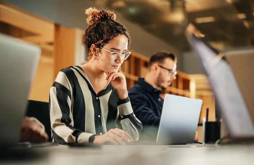 Woman in library working on a laptop. Represents user of VeryConnect's alumni CRM