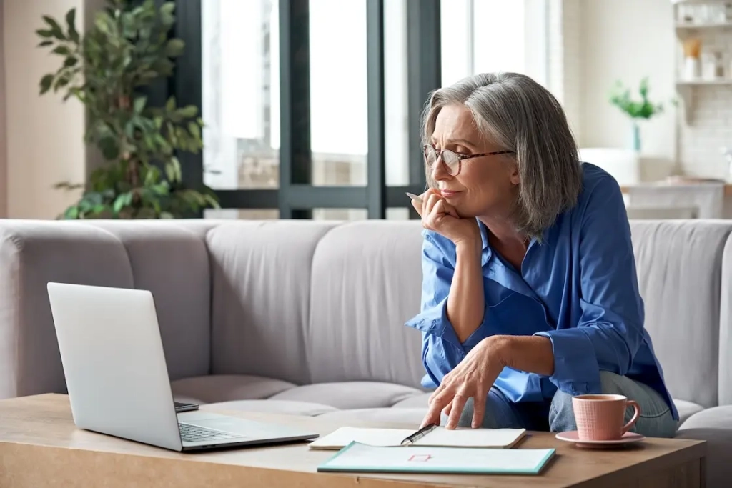 Woman looking at laptop with notepads on desk. Represent's user of VeryConnect's automated invoicing for memberships solution