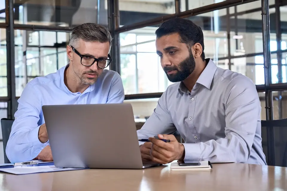 Two professionally dressed men looking at a laptop. Represents user of VeryConnect's corporate mentoring software.