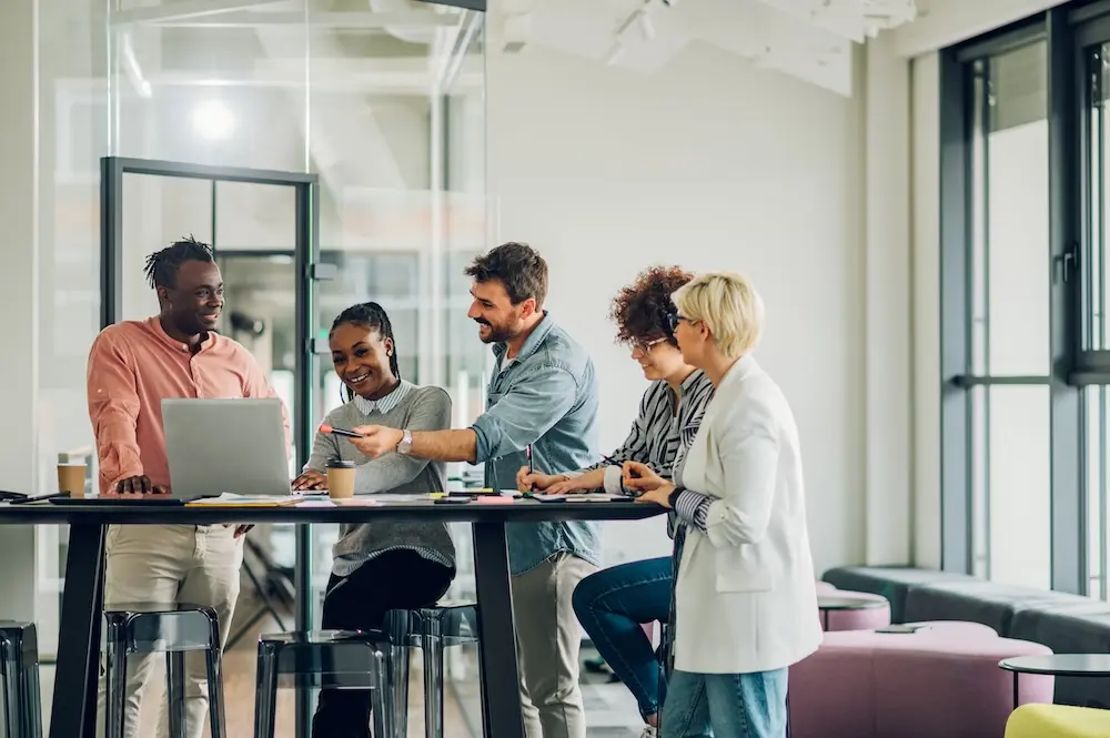 Group of people standing around table looking at laptop. Represents users of VeryConnect's coworking space software.