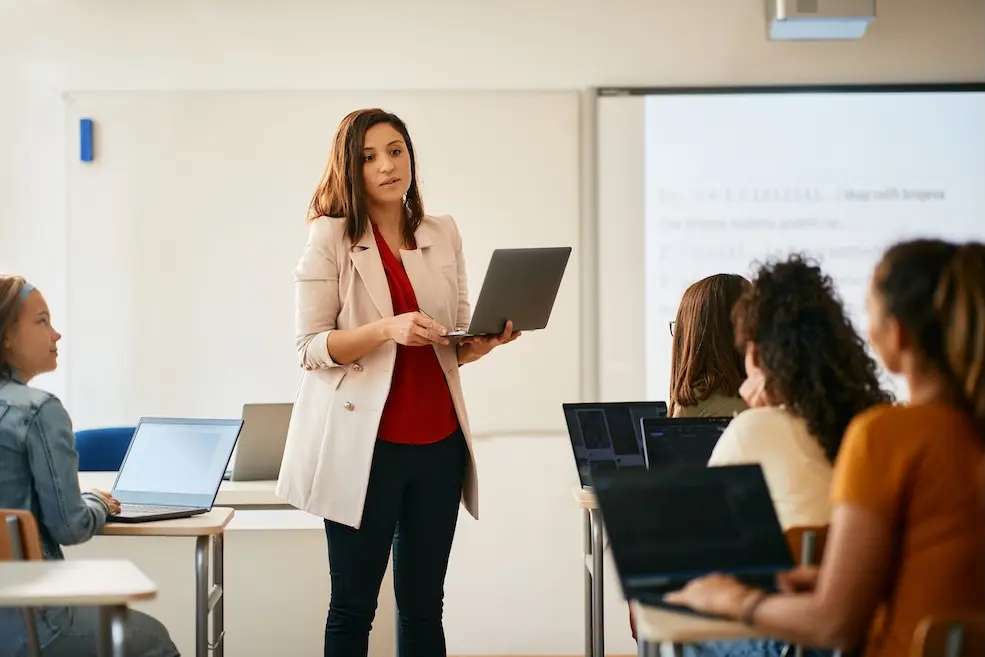 Teacher standing in front of class of people on laptops. Represents user's of VeryConnect's CRM for Educational Institutions