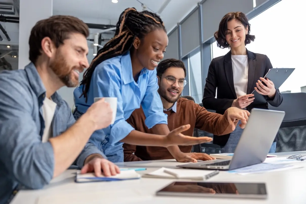 Women showing coworkers her laptop screen. Represents users of VeryConnect's member engagement tools.