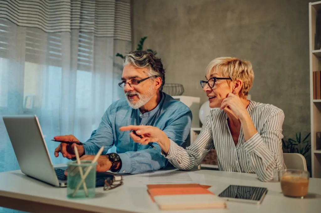 Man and a woman looking and pointing at a laptop, with notebooks and pens on the desk. Represents users of VeryConnect's membership renewal software.