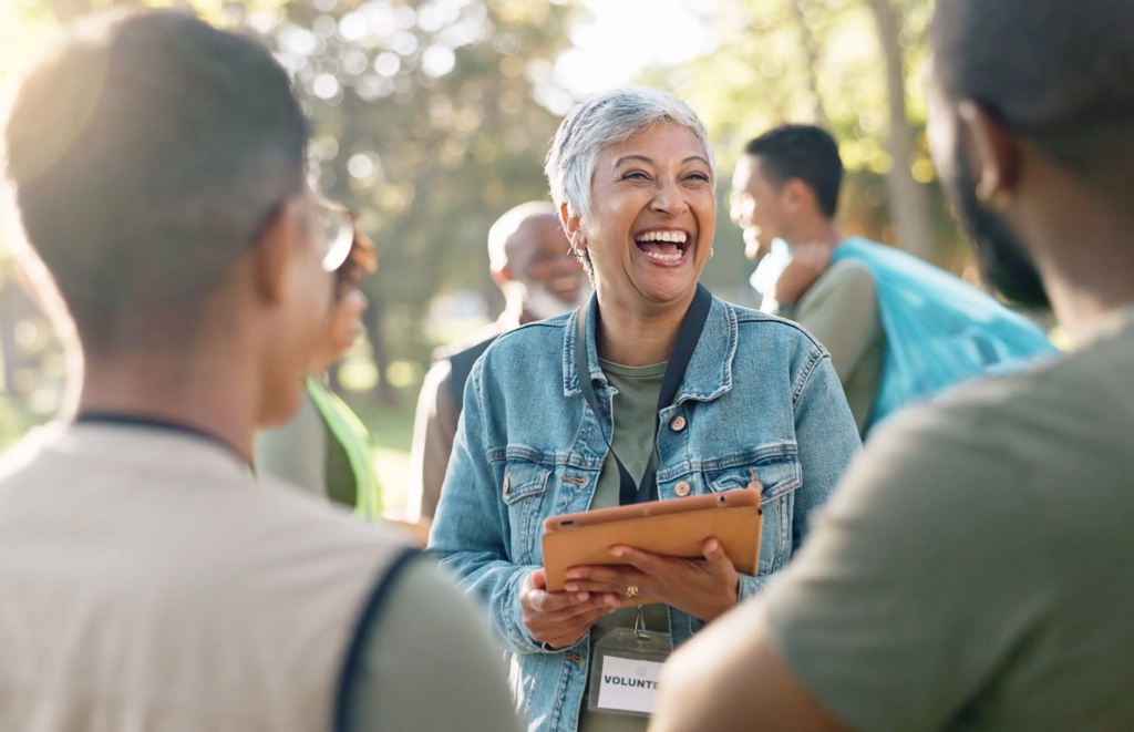 Woman with clipboard smiling at two other people. Represents users of nonprofit software.