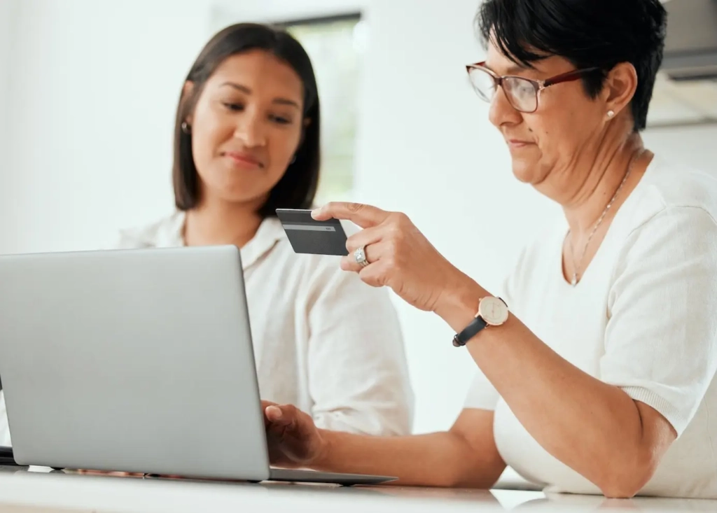 Two women looking at a laptop, one with a payment card in hand. Represents users of VeryConnect's membership payment processing software