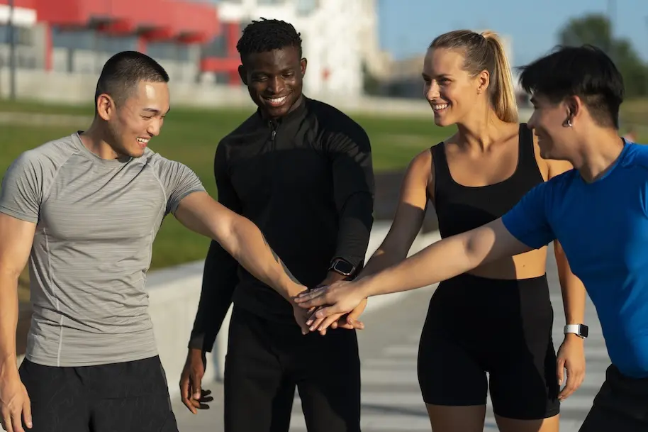 Four people dressed in sports clothes putting their hands in the middle. Represents users of VeryConnect's club management software.