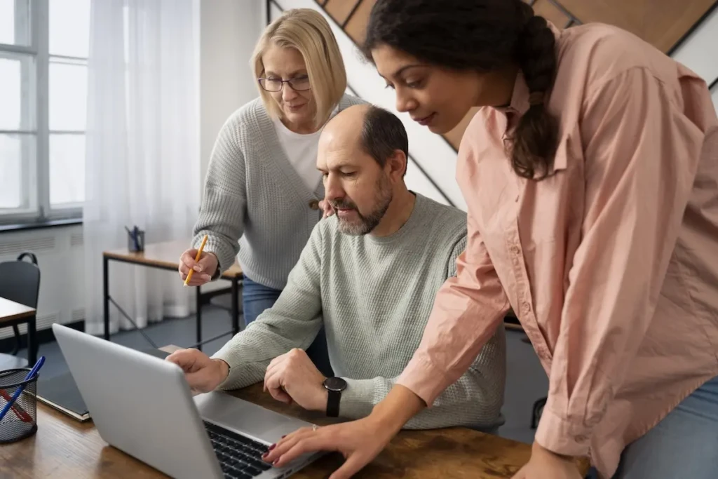 Three people looking at a laptop with one showing them typing. Represents users of VeryConnect's coaching software. Coaching Software