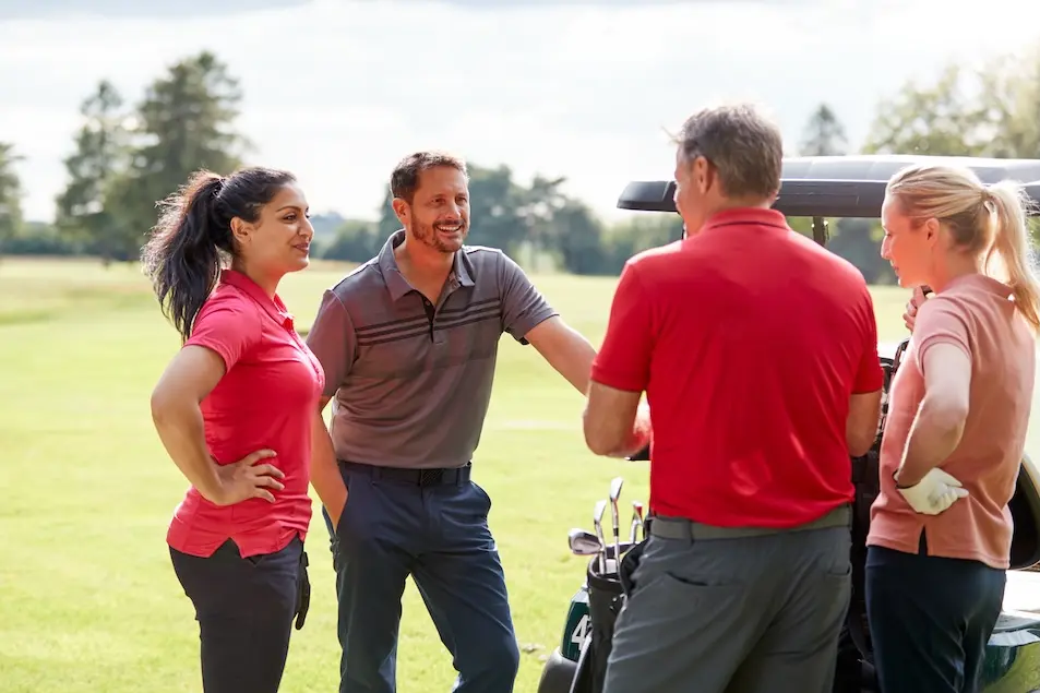 Four people standing at golf cart in conversation, smiling at each other. Represents users of VeryConnect's country club membership software.