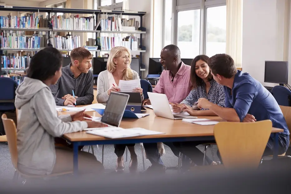 Group of people at desk in library, in conversation. Represents users of VeryConnect's language society membership software.