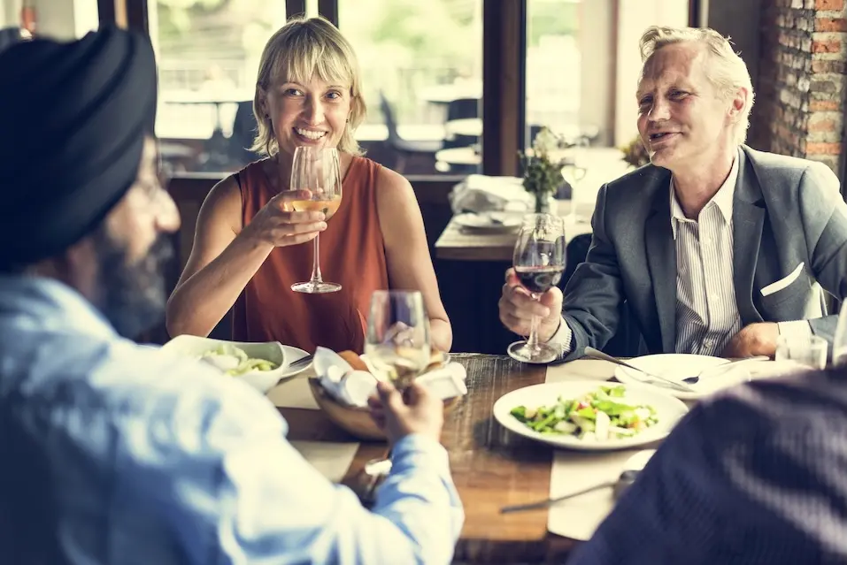 People at a table in a restaurant, holding wine glasses. Represents users of VeryConnect's private members club software.