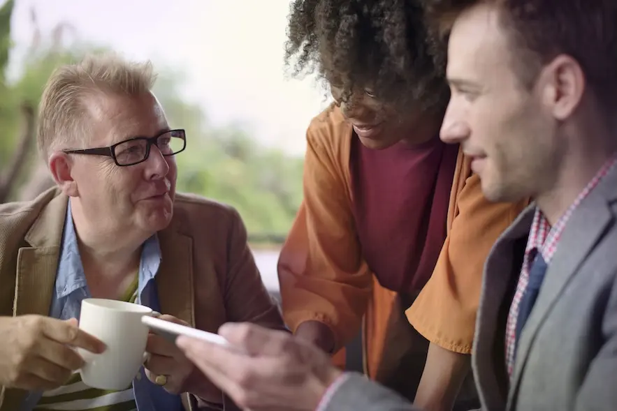 3 people in conversation, looking at ipad. Represents user of guild membership software.