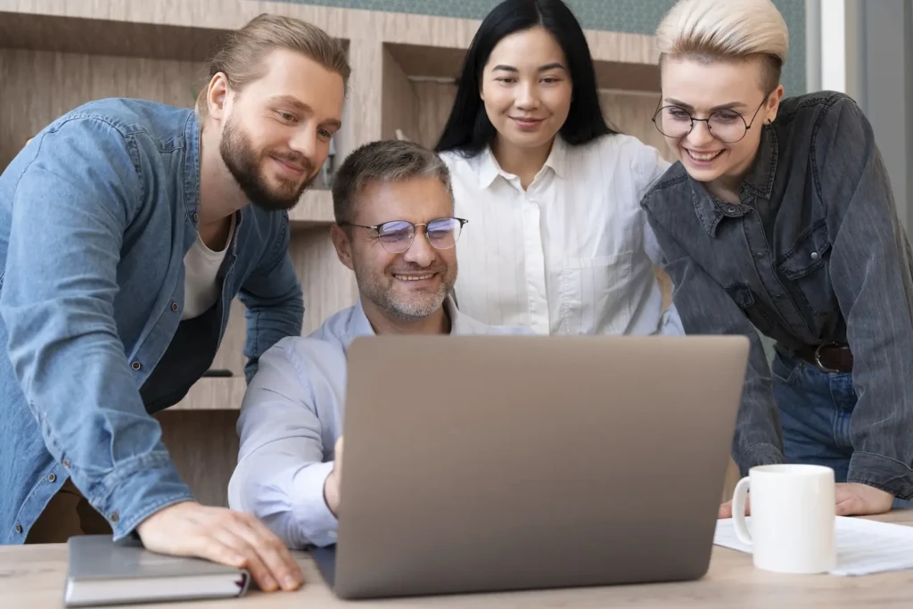 Four people all looking at a laptop and smiling. Represents users of membership website.