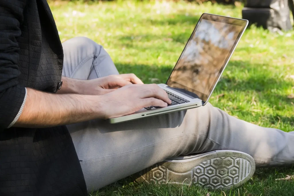 Person sitting on grass, working on laptop.