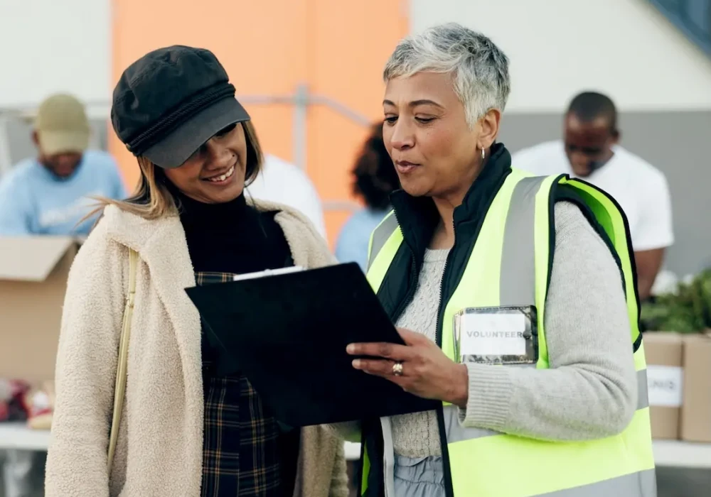 Two women, one with high-vis vest showing the other a clipboard. Represents user of VeryConnect's C charity management software